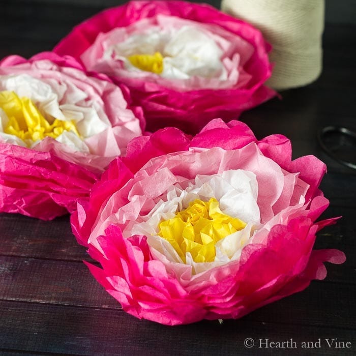 paper flower templates, paper flowers made of pink white and yellow tissue paper, placed on wooden surface