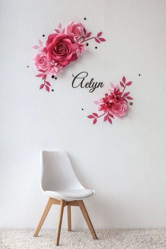 pink paper flowers in different shapes and sizes, arranged on white wall, diy tissue paper flowers, white chair underneath
