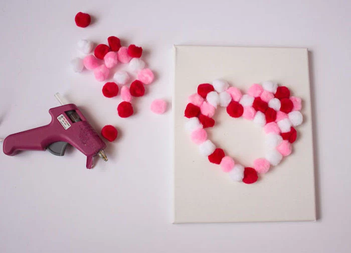 valentine decorations ideas, pink red and white pom poms, glued to a white canvas in the shape of a heart, step by step diy tutorial
