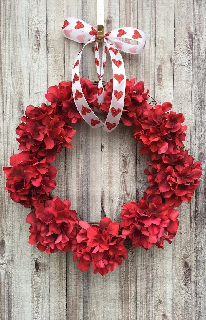 wreath made with red flowers, hanging with white satin ribbon with red glitter hearts, valentine's day home decor