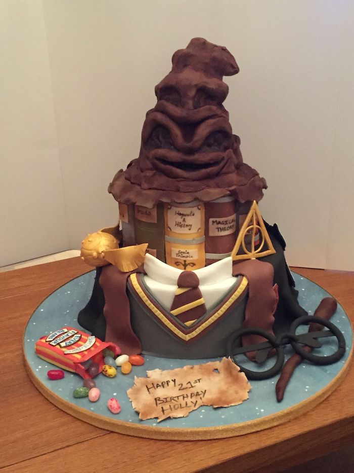 two tier cake with gryffindor uniform, sorting hat made of fondant on top, hogwarts cake, placed on wooden table