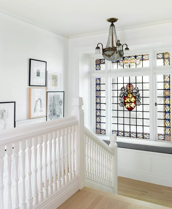 staircase with large window, wooden floors and white railing, stained glass front door, framed art on the wall, vintage chandelier
