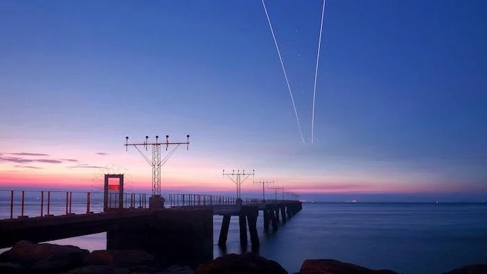 aesthetic computer wallpaper, sunset over a pier, two lines in the sky, airplanes flying above the ocean