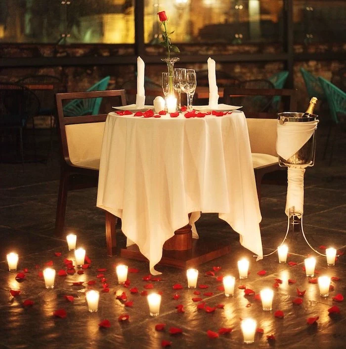 valentine table decorations, dinner table set for two, candles and rose petals scattered on the floor, single rose on the table