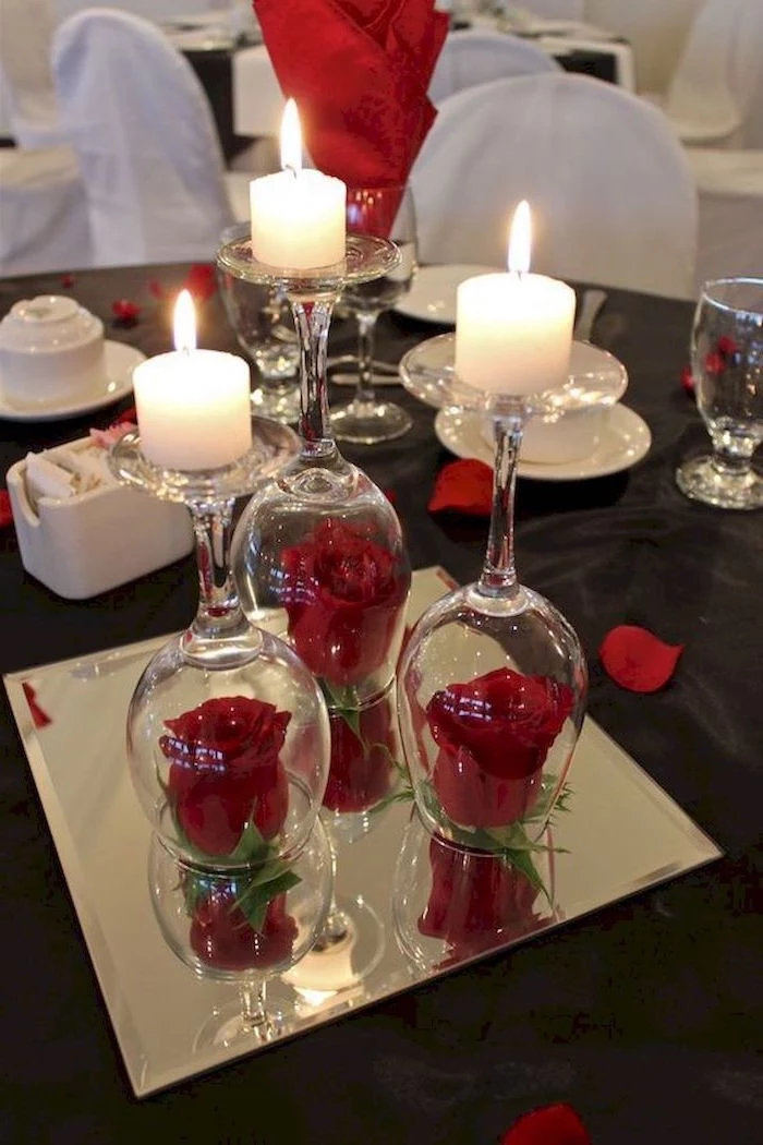 roses covered with wine glasses, candles on top on mirror tray, valentine table decorations, dinner table set for two