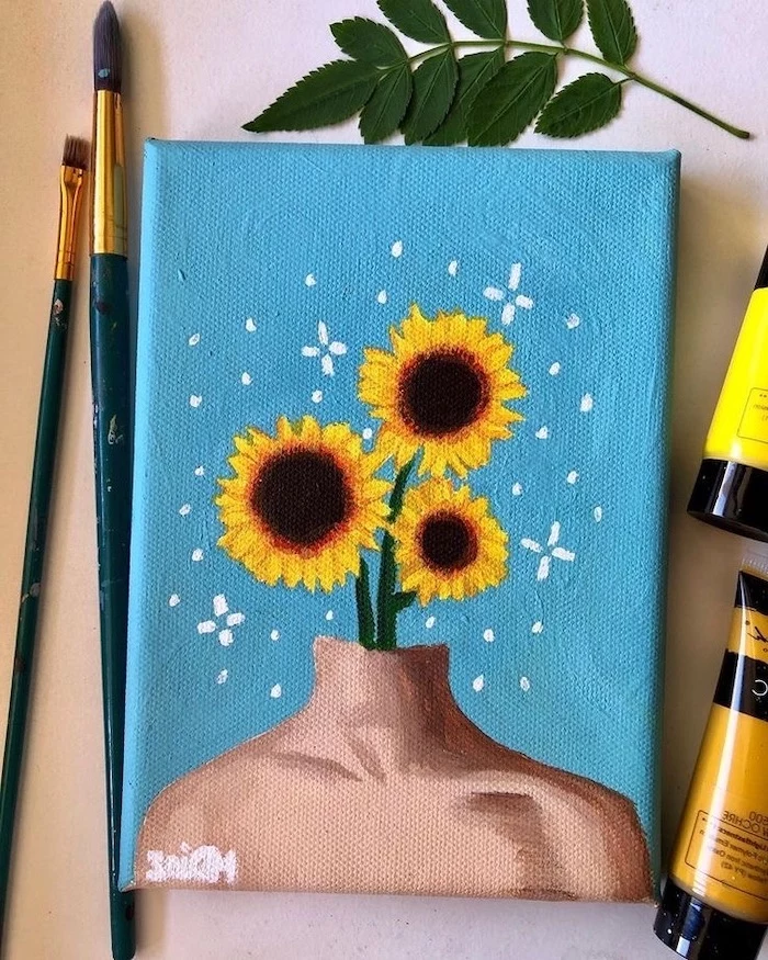 three sunflowers coming out of a mannequin, acrylic painting ideas for beginners on canvas, blue background, brushes around it