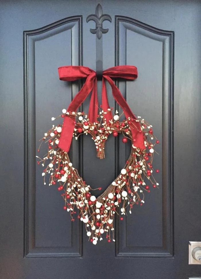 heart shaped wreath, made of twigs and faux berries, hanging on black door with red satin bow, valentines home decor