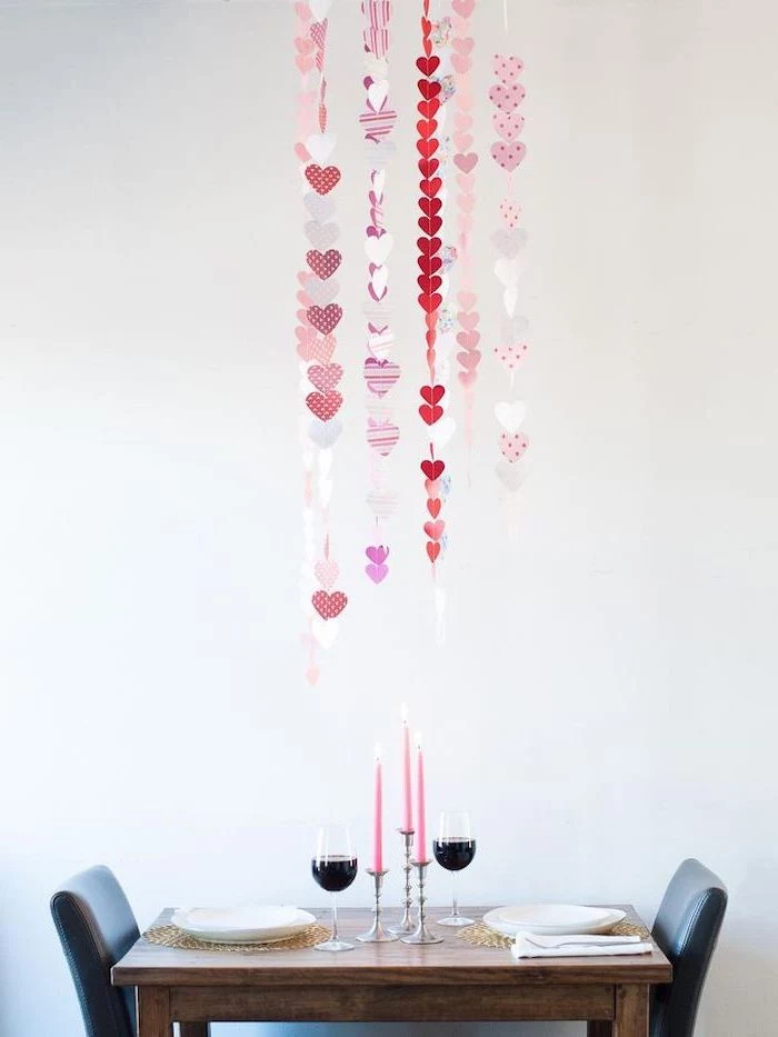 dinner table set for two, hearts garlands, hanging from the ceiling, valentines home decor, wine glasses and pink candles