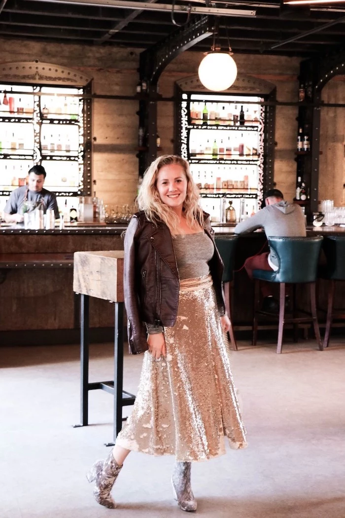 woman standing at a bar, wearing gold sequinned skirt, grey crop top and leather jacket, valentines day outfit girl
