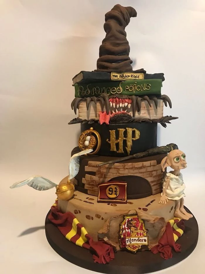 multi layered cake, sorting hat on top, wand dobby and golden snitch on the side, diy harry potter cake, gryffindor scarf around it