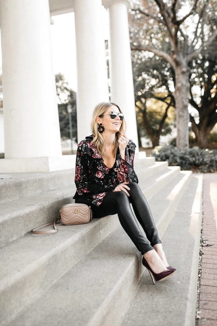 woman sitting on stairs, valentines day outfit ideas, wearing black leather pants, floral blouse and sunglasses
