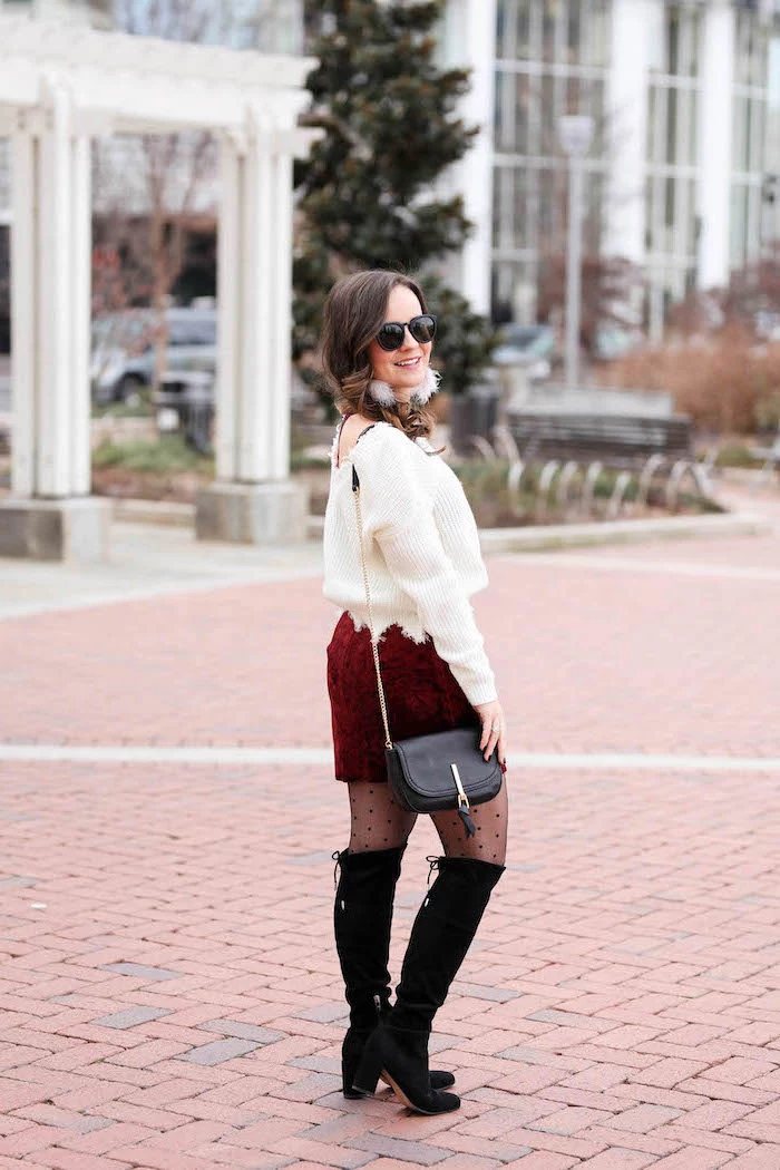 woman standing on sidewalk, what to wear on valentine's day, wearing red velvet skirt, white sweater, black boots and bag