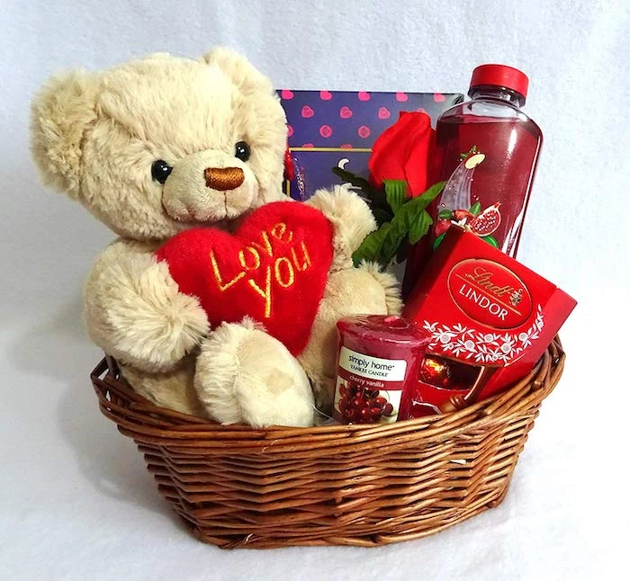 wooden basket, filled with candies and plush teddy bear, valentine's day gift ideas for her, placed on white surface