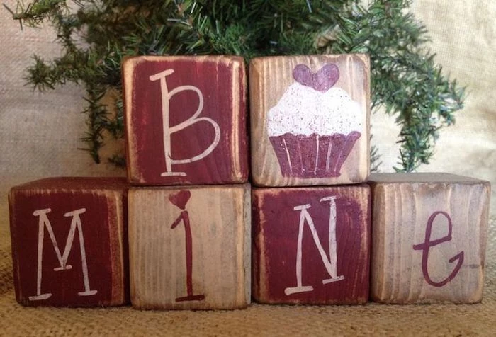 be mine wooden cubes, painted in red, valentine day table decorations, green tree branches in the background