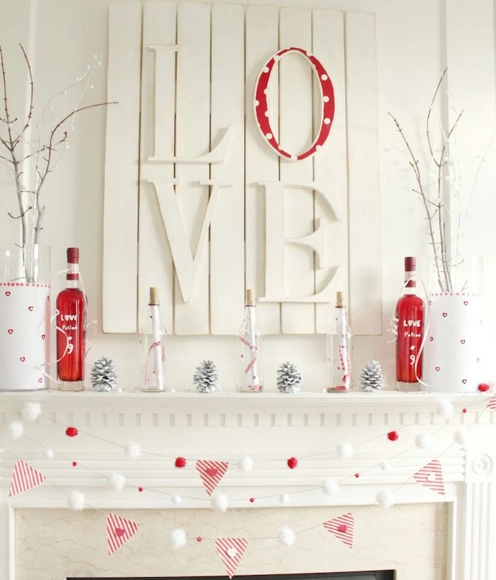white wooden love board, garlands hanging over mantel, bottles painted in red, pine cones, arranged on shelf, valentine day table decorations