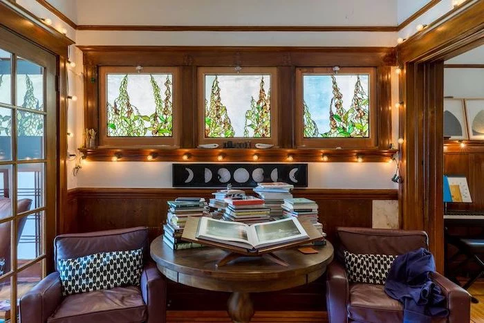reading room with wooden window and door frames, custom stained glass windows, brown leather armchairs, round table with books