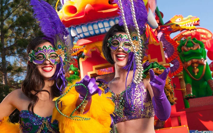 mardi gras mask, two women wearing mardi gras costumes, throwing beads at the carnival, masks with large feathers