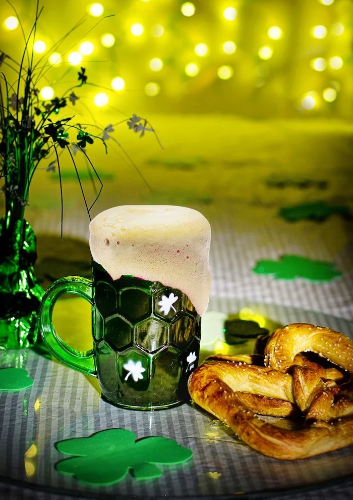 beer in green mug with white shamrocks, placed on a table, st patrick's day decorations, fairy lights in the background