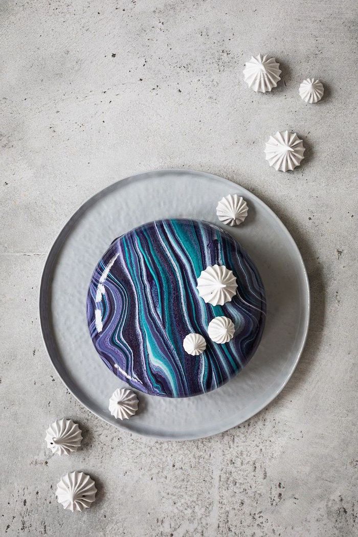 blue purple and white glaze on one tier cake, placed on grey cake tray, mirror glaze cake, meringue kisses around it