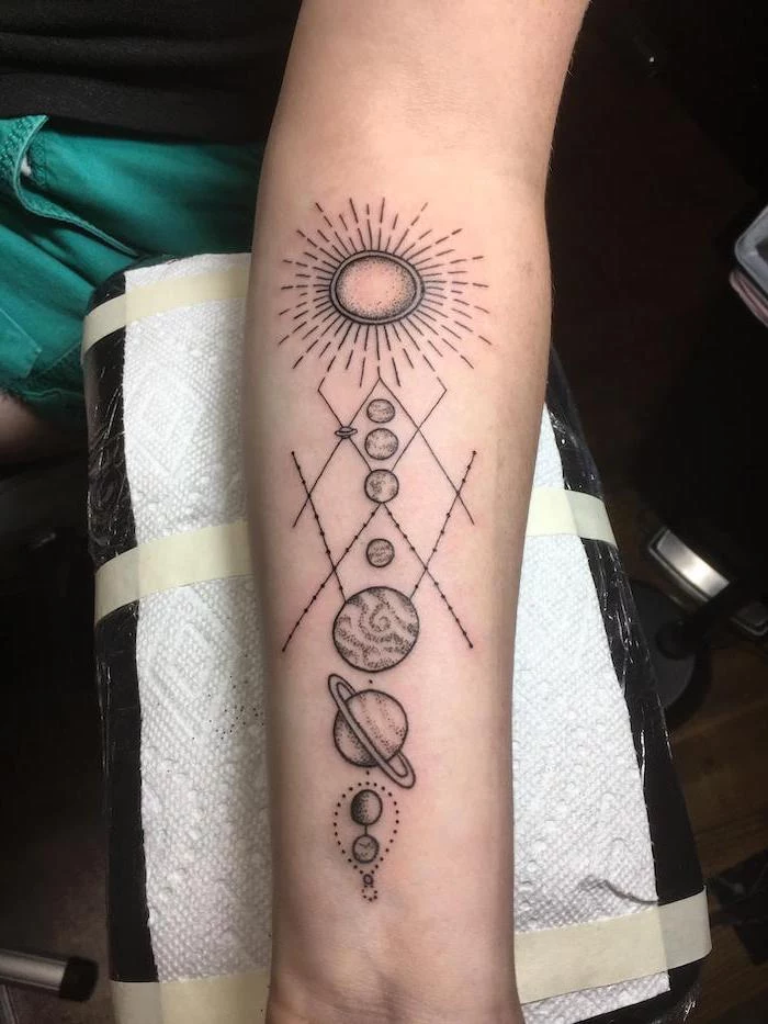 forearm tattoo, sun and planets in a line, moon and stars tattoo, hand leaning on leather stool wrapped with white paper