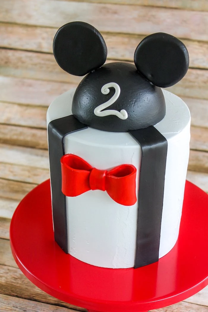 one tier cake, covered with white fondant, decorated with black and red fondant, mickey mouse cake, placed on red cake stand