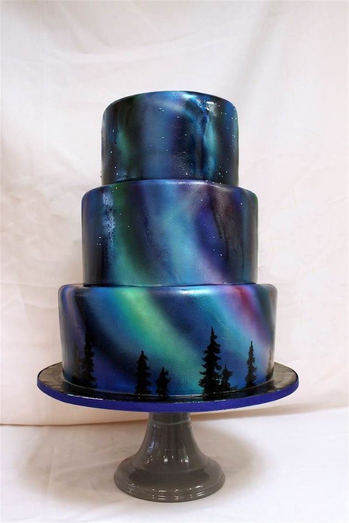 three tier cake, galaxy cake, northern lights colored glaze, placed on dark grey metal cake stand, white background