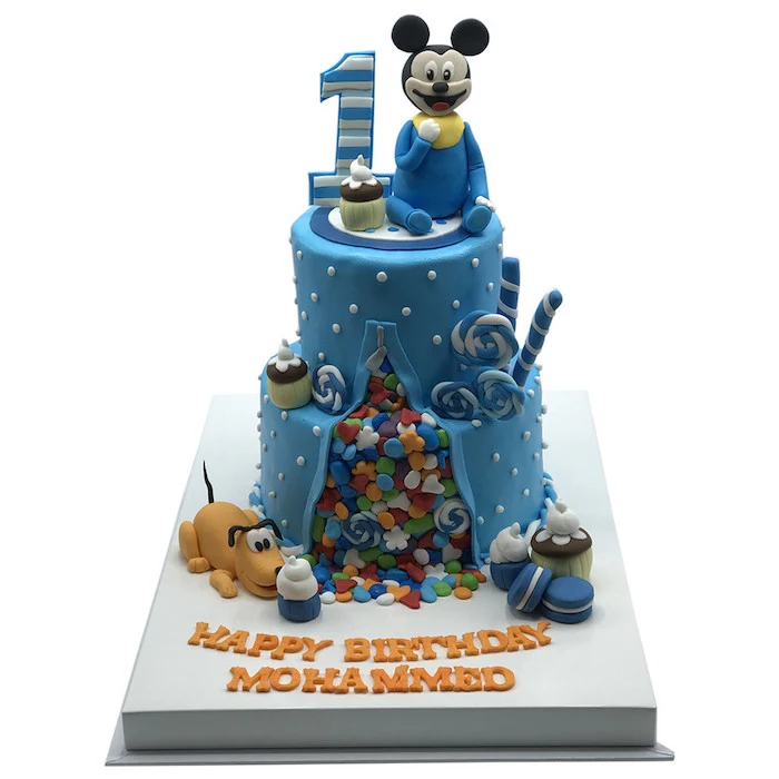 two tier cake, covered with blue fondant, mickey mouse birthday cake, fondant candy spilling out of the cake