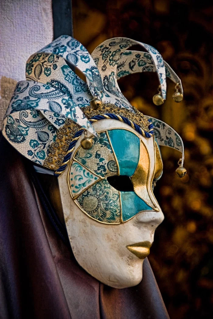 black masquerade mask, white mask decorated in gold and blue, lips painted in gold, bells at the end