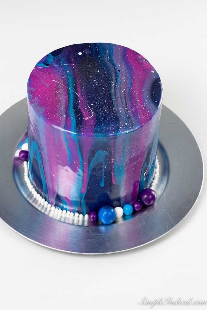 galaxy cake, blue pink and purple mirror glaze on one tier cake, placed on metal cake tray, candy decorations around it