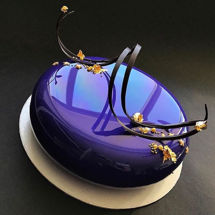 one tier cake with purple glaze on top, mirror glaze, black and gold decorations on top, placed on white cake tray