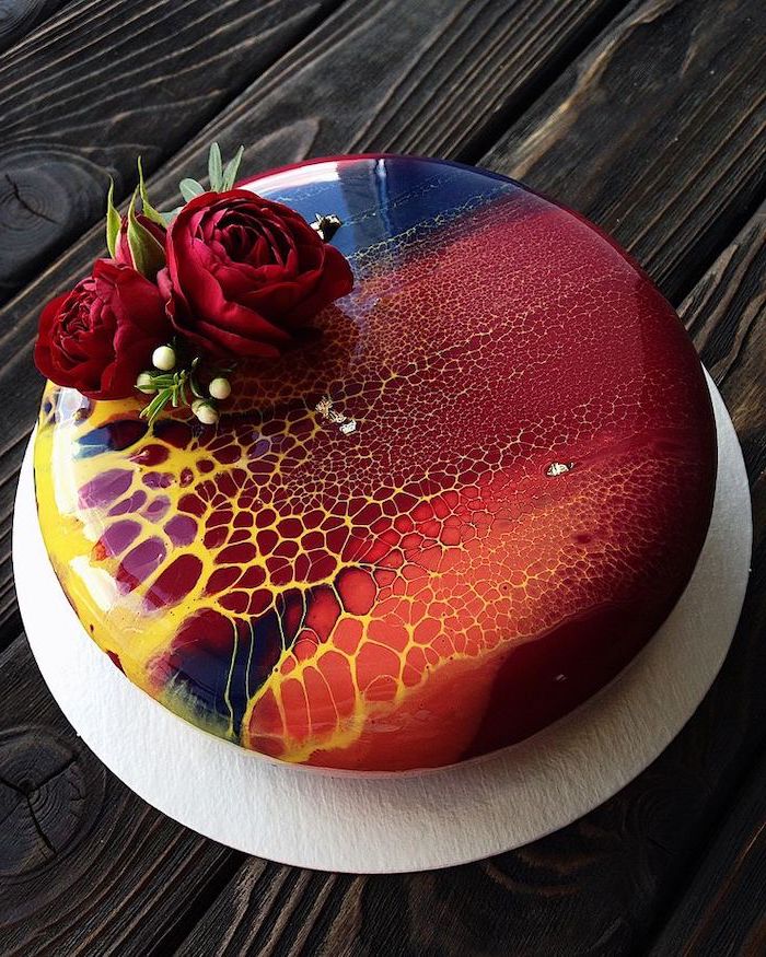 read orange blue and yellow glaze on one tier cake, mirror glaze, two red roses on top, placed on white cake tray
