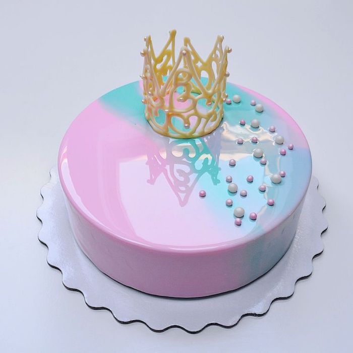 pink and blue glaze on one tier cake, mirror glaze, candy pearls and crown on top, placed on white cake tray
