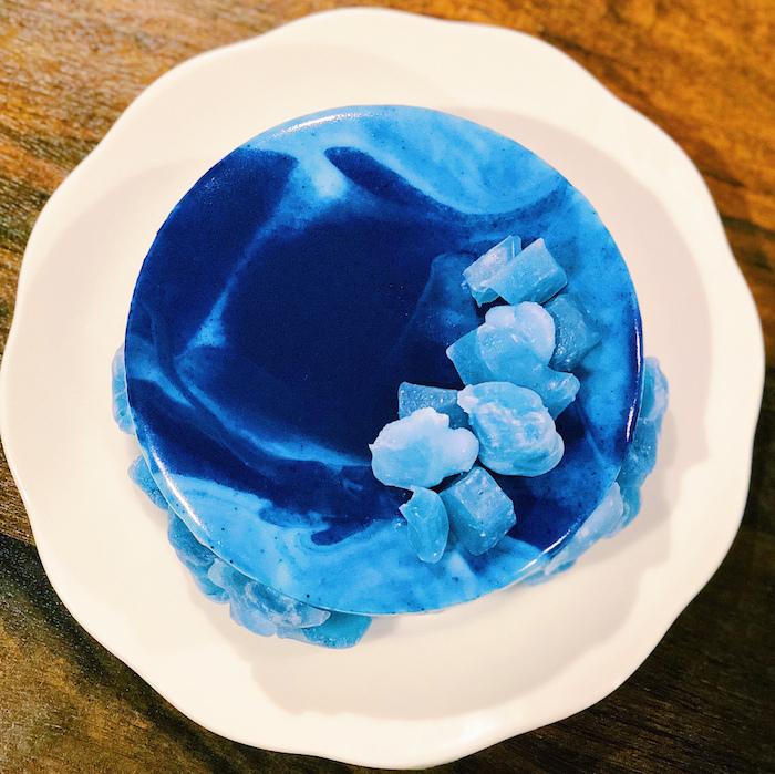 mirror glaze recipe, one tier cake, covered with marble shades of blue glaze, rock candy decorations on top, placed on white plate