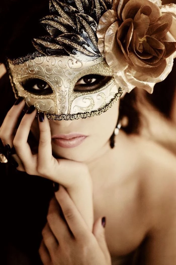 woman wearing gold mask, decorated with glitter, plastic rose on the side, black masquerade mask