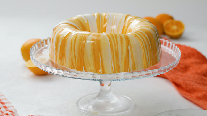 one tier donut cake, covered with white orange and yellow glaze, placed on glass cake stand, mirror glaze recipe