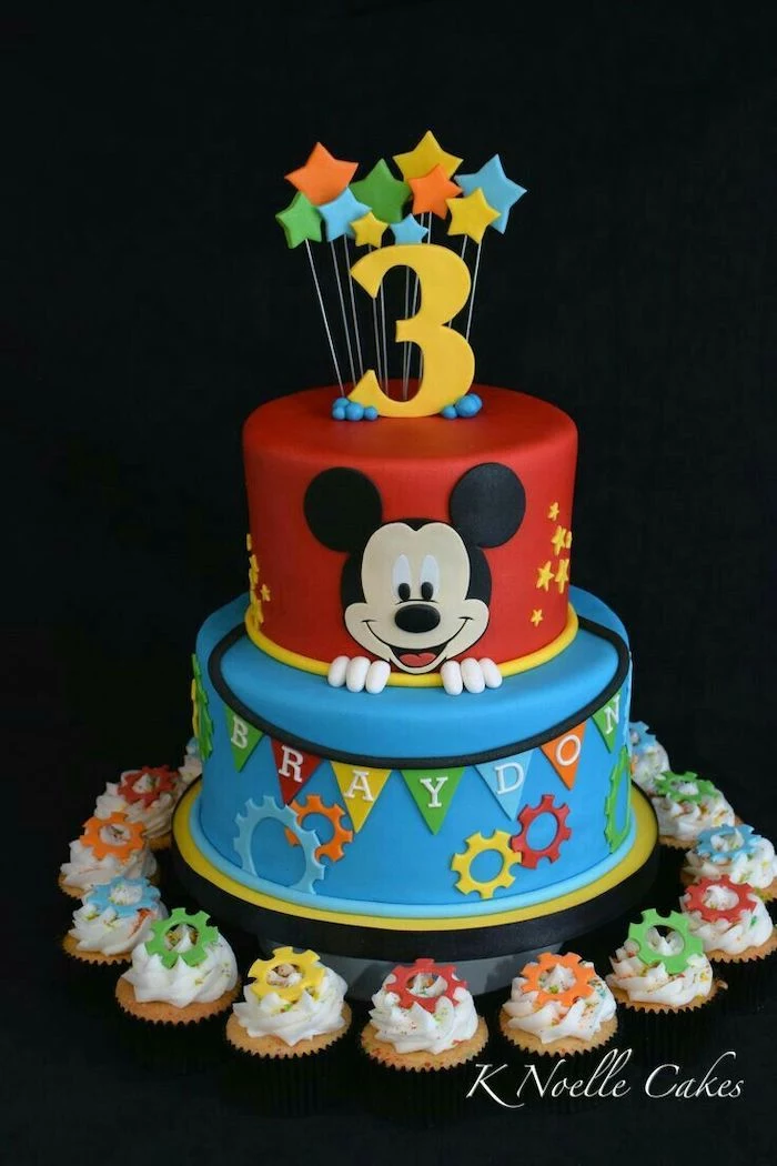 mickey mouse cake ideas, two tier cake, covered with red and blue fondant, cupcakes arranged around it