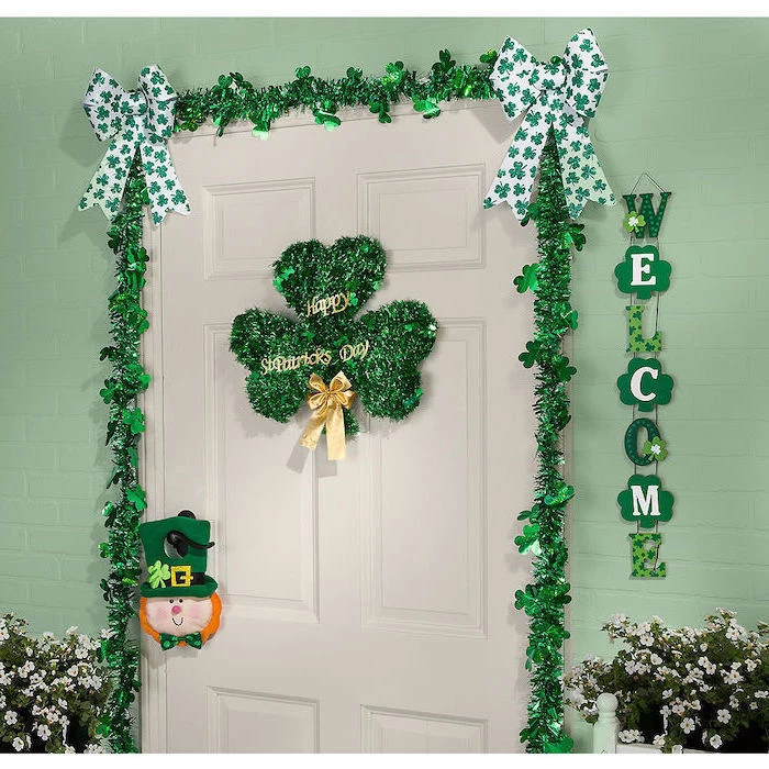 white wooden door, st patricks day wreath, decorated with green garland, two green and white ribbons in the corners