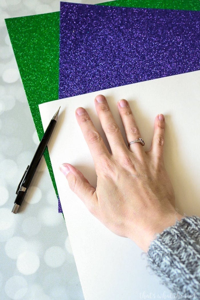 purple and green glitter paper, masquerade ball masks, female hand placed on a sheet of paper, to be traced with pencil