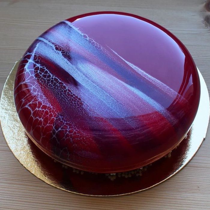 cake glaze recipe, one tier cake covered with red and white blue glaze, placed on a gold cake tray, placed on wooden surface