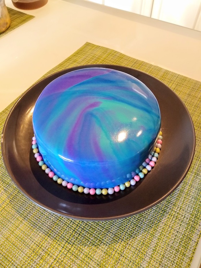 one tier cake with blue green and purple glaze, cake glaze recipe, candy arranged around it, placed on black plate