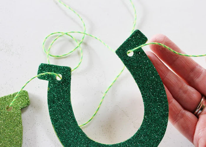 green glitter horseshoe, held together by green and yellow thread, st patrick's day crafts, step by step diy tutorial