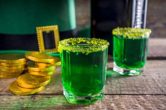 green drink in a glass, yellow sugar around the rim, placed on wooden table, st paddy's day, gold coins around it