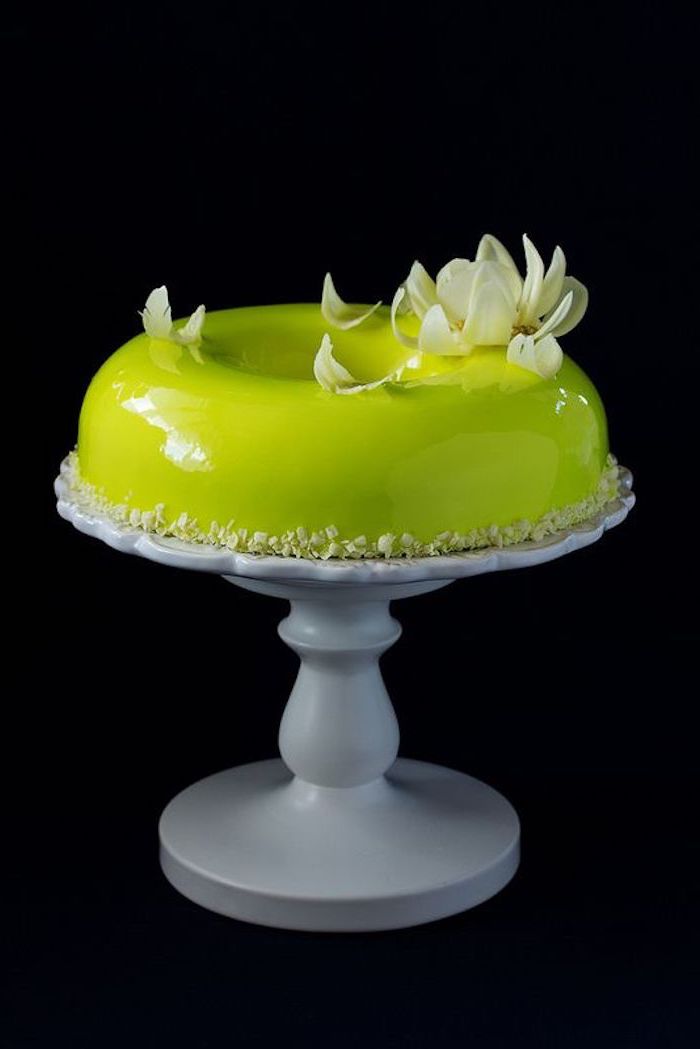 one tier donut cake, covered with green glaze, placed on white cake stand, white flower decorations on top, chocolate mirror glaze