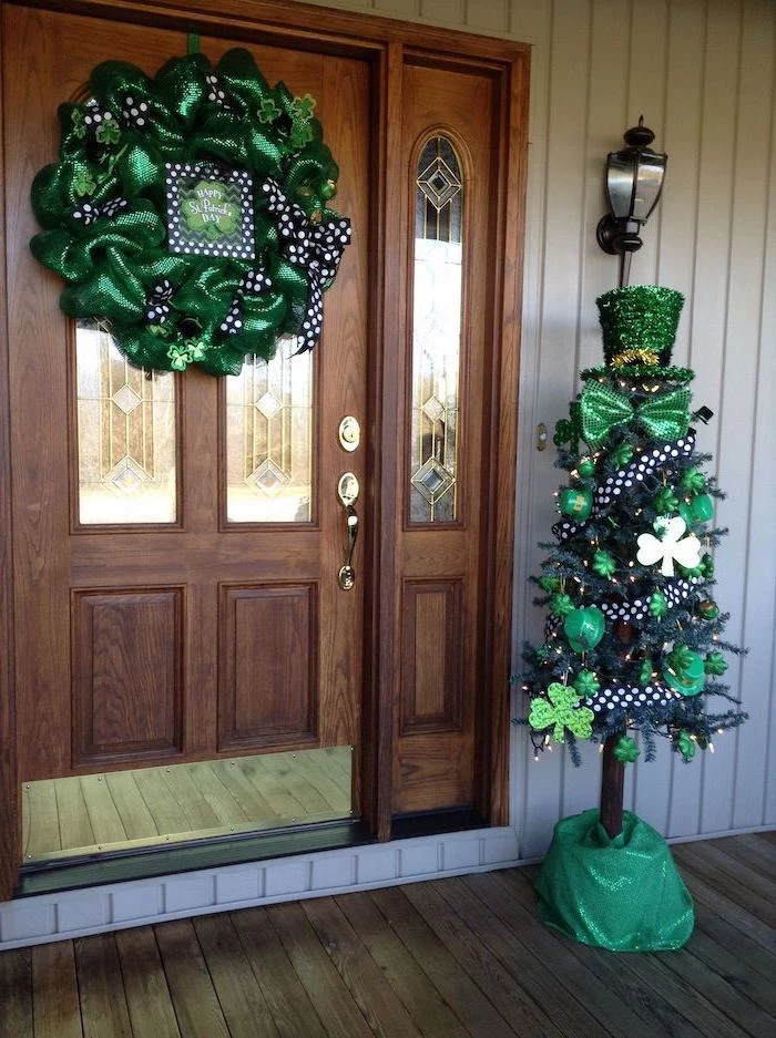 large wooden door, wreath with green tulle, decorated with black and white ribbons, decorated tree on the side, happy st patrick's day