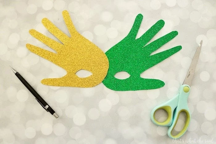 two handprints, made of gold and green glitter paper, masquerade masks for women, connected together