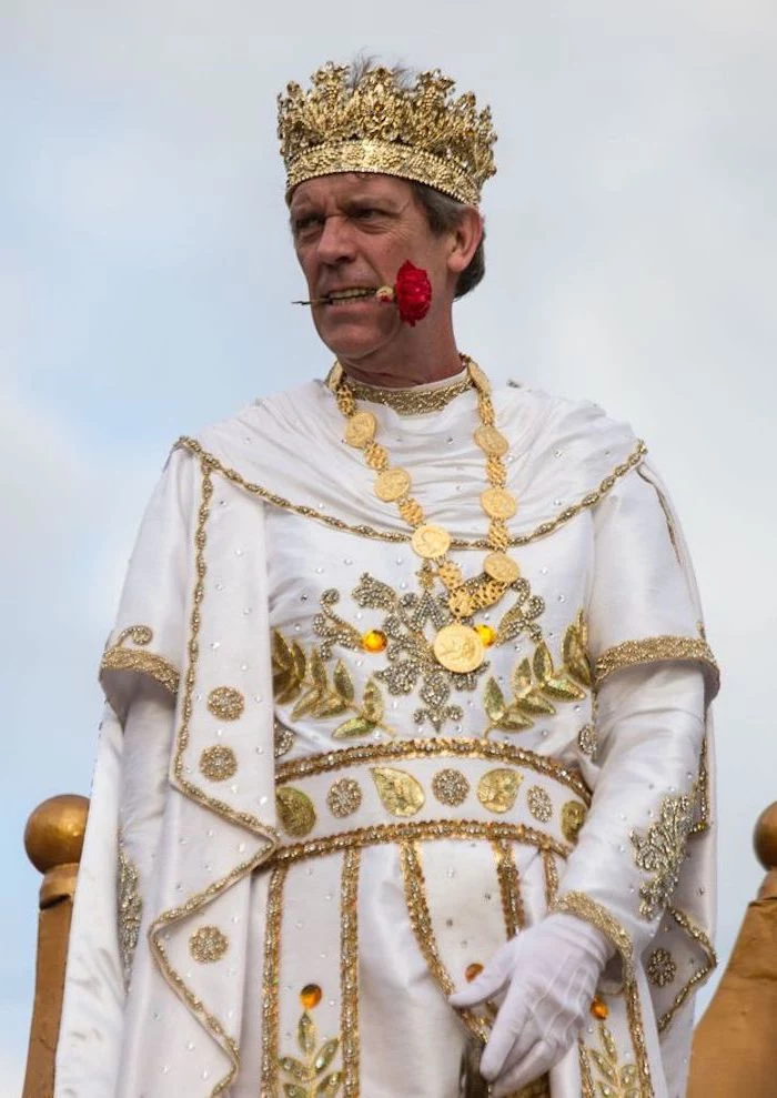 hugh laurie as king bacchus, masquerade masks, wearing white and gold costume, gold crown on his head