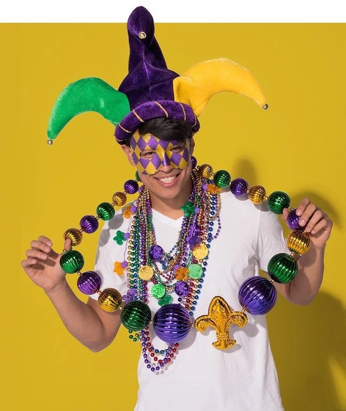 man wearing lots of beads necklaces, masquerade ball masks, purple and gold mask, purple gold and green jester hat