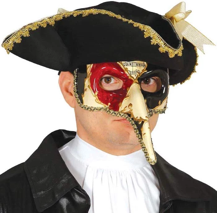 man wearing black hat with gold decorations, masquerade decorations, white mask with red and black paint around the eyes