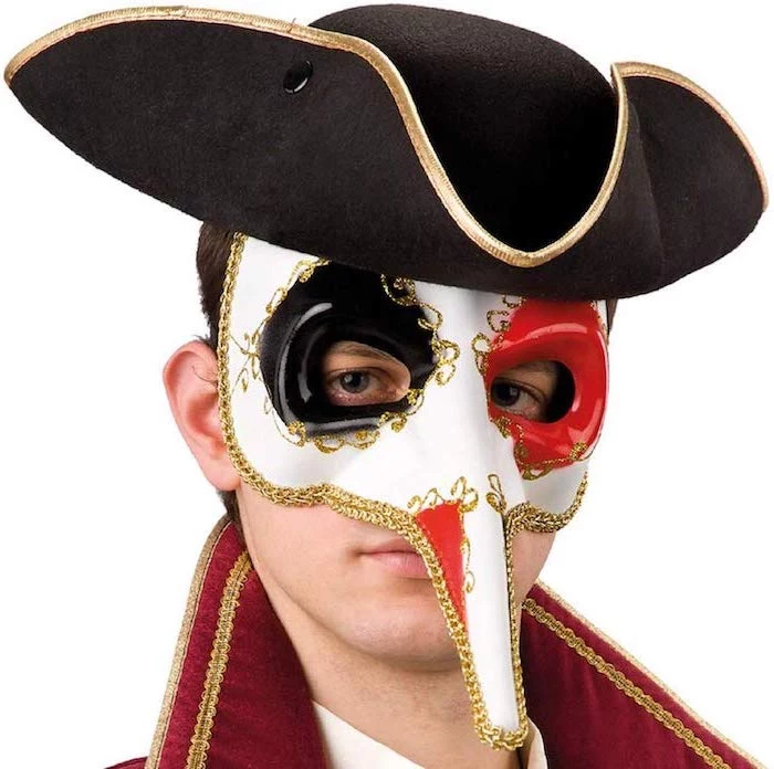 man wearing a black hat, white mask with gold decorations, red and black paint around the eyes, masquerade decorations