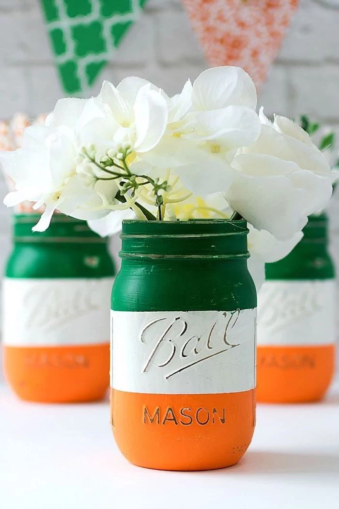 mason jars painted in the colors of the irish flag, st patricks decor, green white and orange, white faux flowers inside